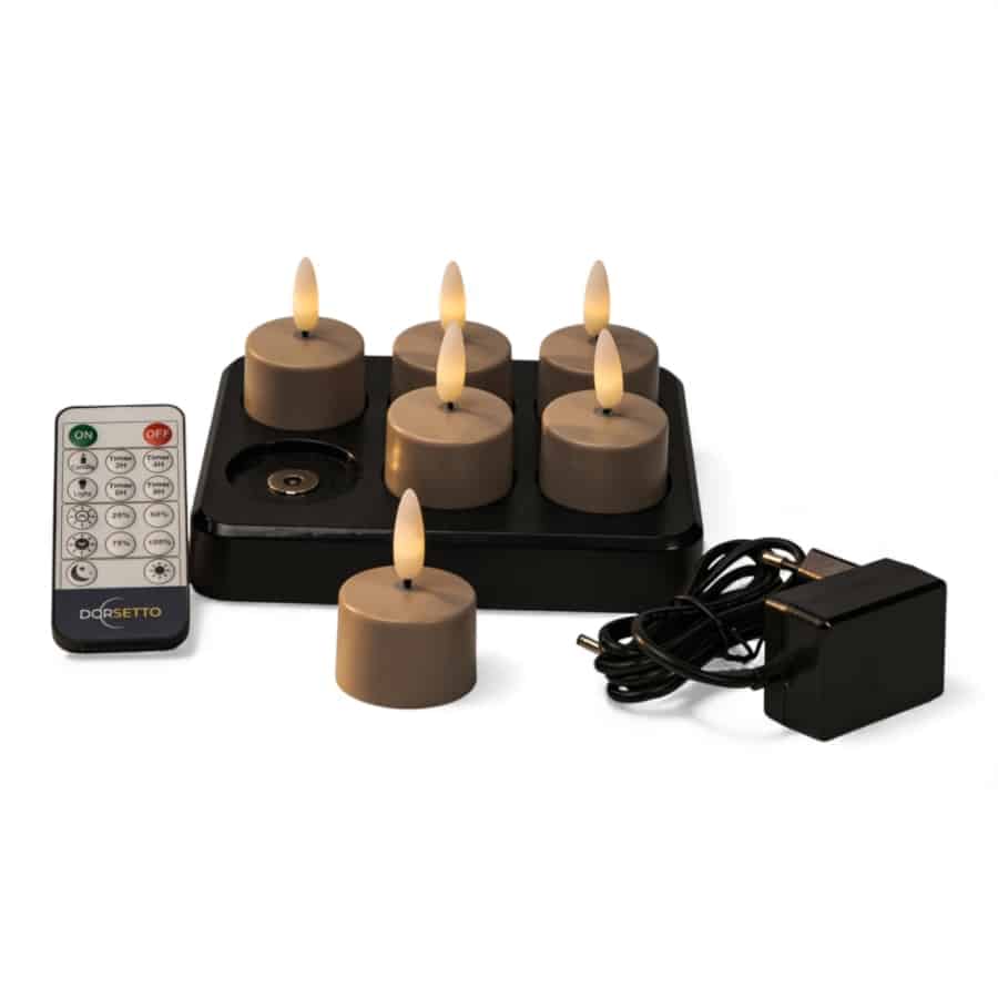 Een set van zes bruine vlamloze LED theelichtkaarsen op een zwart oplaadplateau, met een afstandsbediening en een zwarte voedingsadapter ernaast geplaatst.