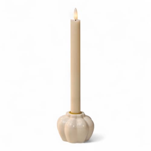 Een brandende beige conische kaars staat in een glanzende, ronde houder van geribbeld keramiek op een effen witte achtergrond.